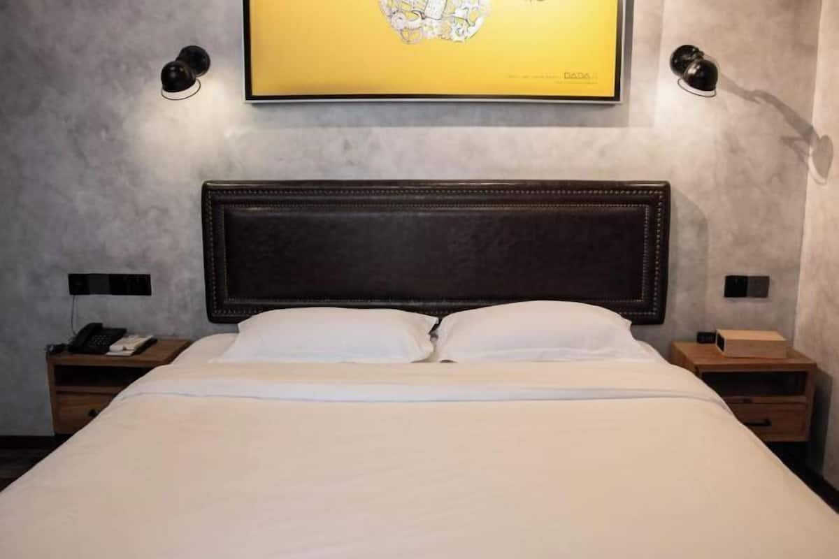Habitación de hotel con una cama grande, cabecera oscura, dos mesitas de noche con lámparas y un cuadro en la pared.
