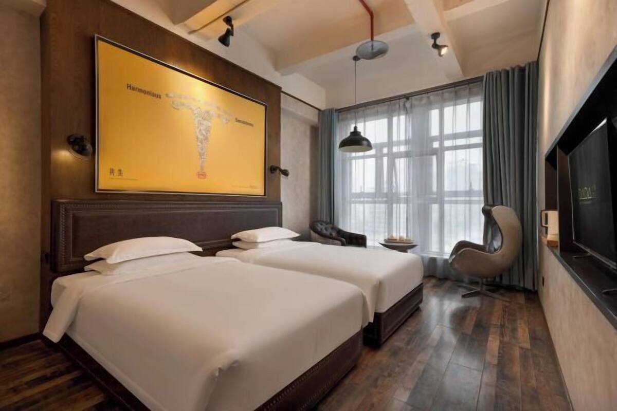 Habitación de hotel con dos camas, un mapa grande enmarcado en la pared, un televisor y una ventana con cortinas.