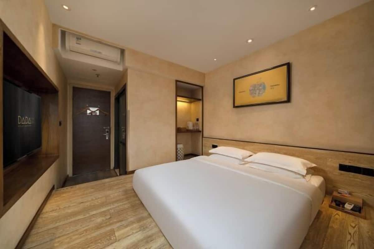 Una habitación de hotel moderna con una cama grande, un televisor de pantalla plana, un cuadro enmarcado en la pared y piso de madera.