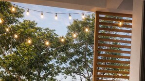 Une terrasse en bois avec deux chaises longues, une plante en pot et des guirlandes lumineuses.