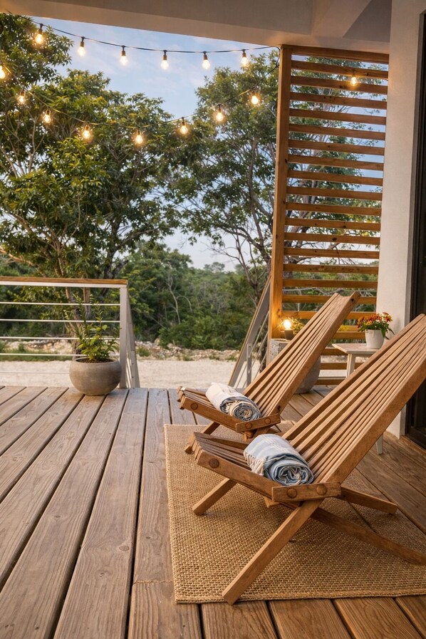 A wooden deck with two lounge chairs, a potted plant, and string lights.