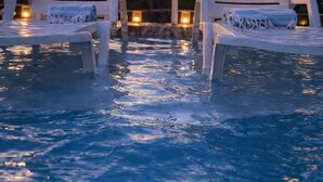 Deux fauteuils de relaxation blancs, placés au bord d’une piscine, avec vue sur le coucher de soleil.