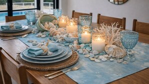 Une table à manger dressée avec des assiettes, des couverts, des bougies et des coquillages décoratifs.
