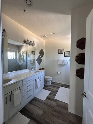 A modern bathroom with a large mirror, two sinks, a toilet, and decorative wall art.