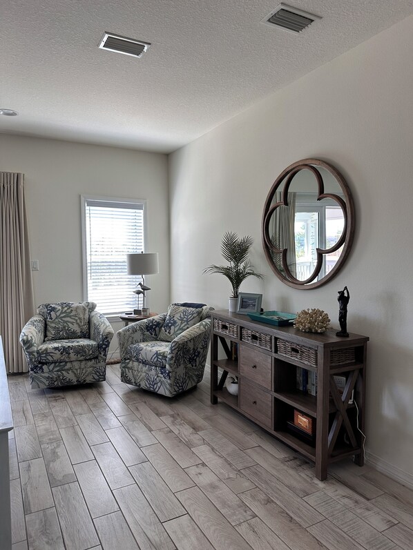 A living room with two patterned armchairs, a wooden console table with decorative items, and a large mirror on the wall.