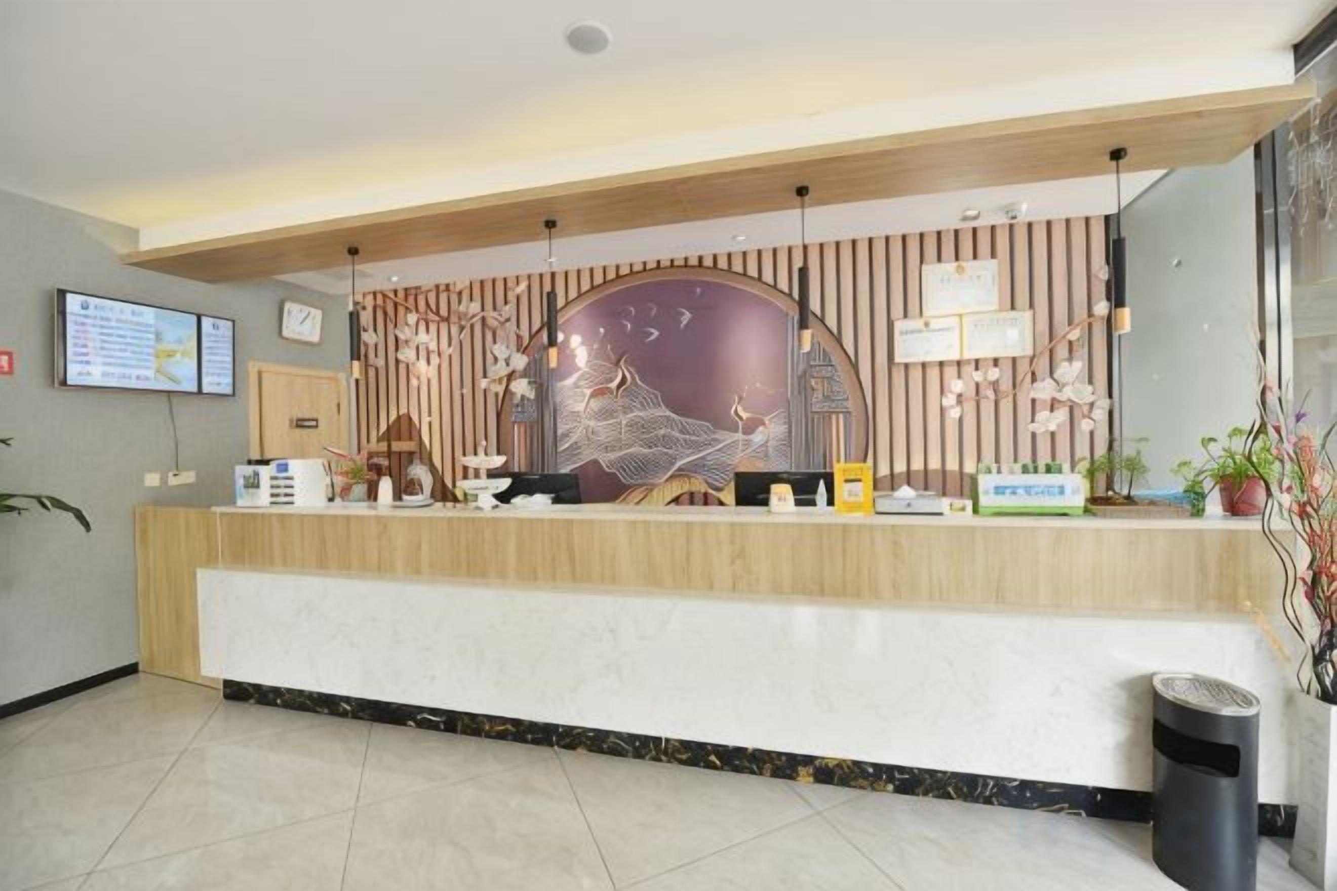 Un comptoir d’accueil au design moderne, un écran numérique et une plante en pot.