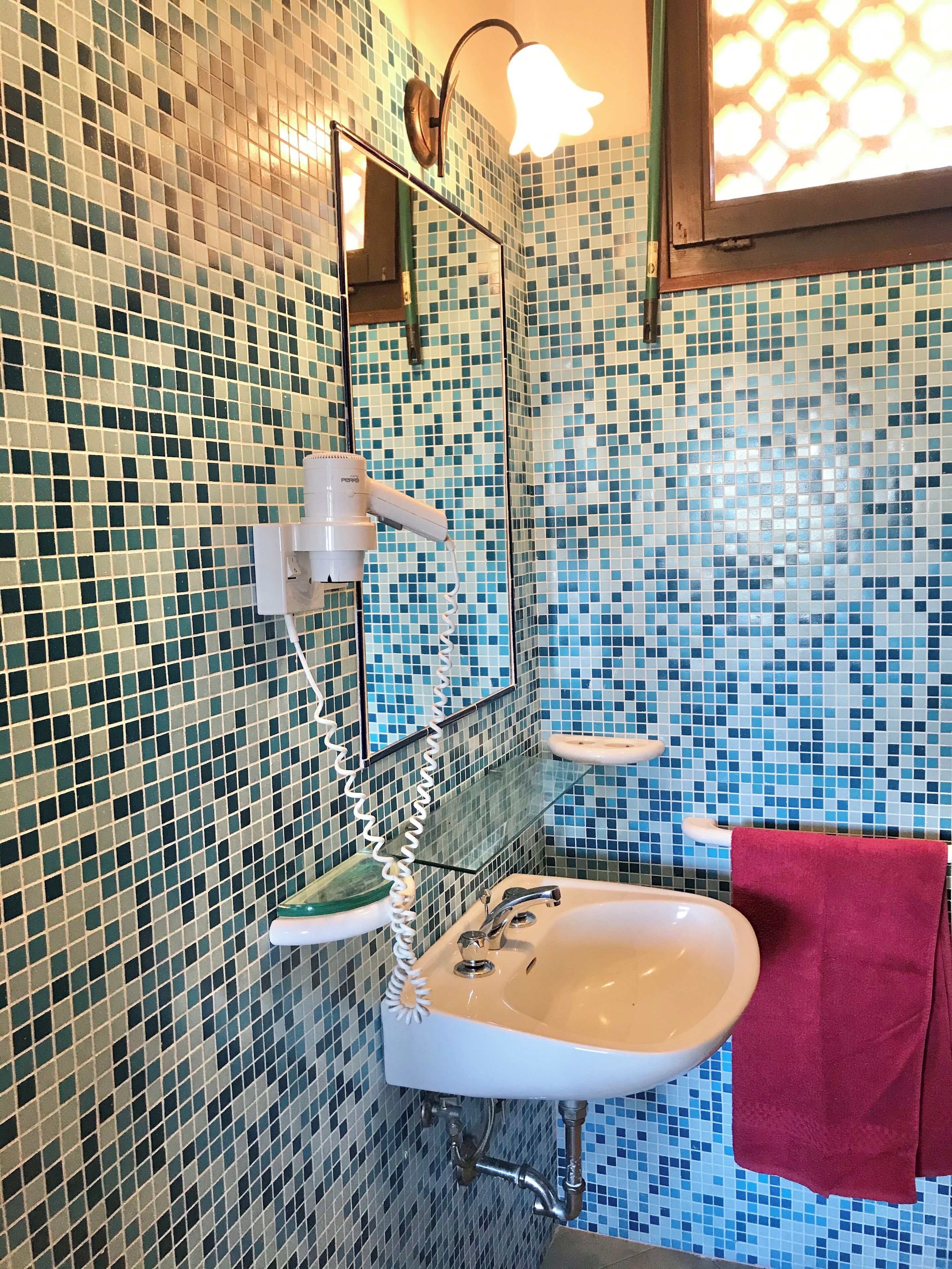 A bathroom with a sink, mirror, and a shower head mounted on the wall.