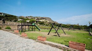 A park with a playground, stone pathway, and houses in the background. - Residence in Stintino 50 mt from the sea (Stintino)
