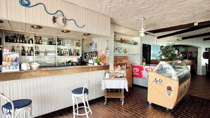 A bar area with stools, a counter with various bottles, a life preserver decoration, and a dessert display. - Residence in Stintino 50 mt from the sea (Stintino)