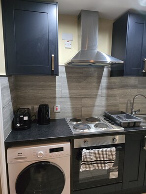 Compact kitchen with washing machine, oven, coffee maker, and sink for self-catering convenience.