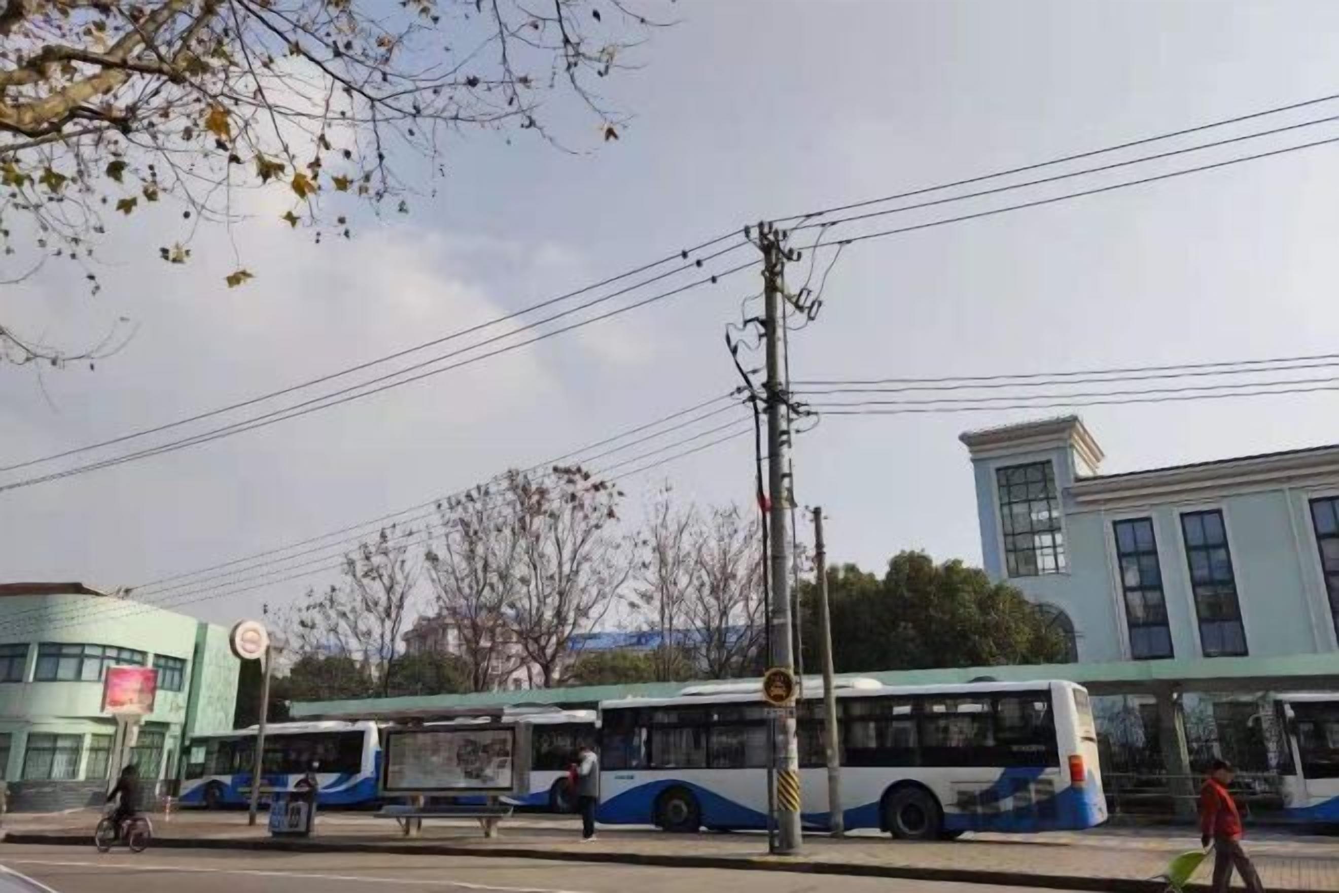 Una parada de autobús con un autobús, un peatón y un edificio al fondo.