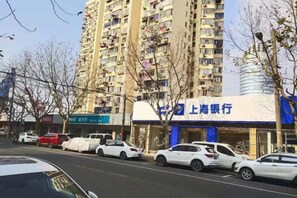 A multi-story residential building with balconies, a bank, and parked cars on the street. - 99 Inn Preferred Hotel (Shanghai Wulian Road Subway Station) (Shanghai)