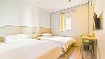 Quarto de hotel com duas camas, uma pequena escrivaninha, um espelho e uma janela com cortinas.