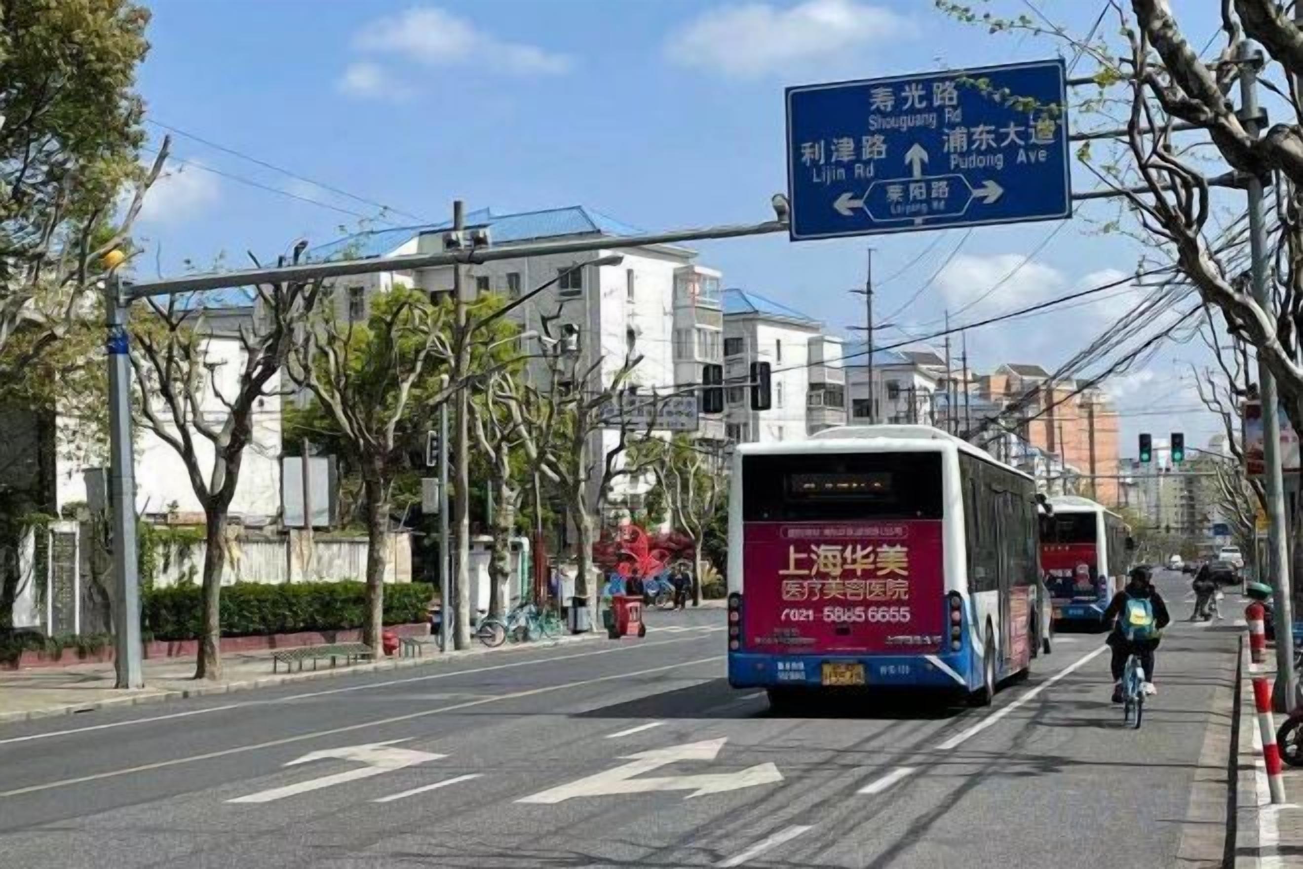 A street with a bus and a cyclist. There is a blue directional sign above the road.