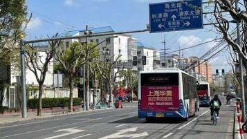 A street with a bus and a cyclist. There is a blue directional sign above the road.