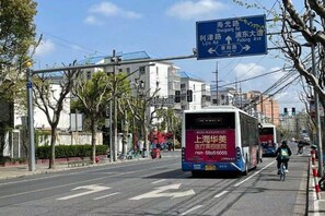 A street with a bus and a cyclist. There is a blue directional sign above the road. - 99 Inn Preferred Hotel (Shanghai Wulian Road Subway Station) (Shanghai)