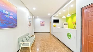Uma área de recepção de hotel com balcão, um banco e uma TV fixada na parede.