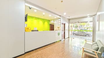 Uma área de recepção de hotel, com balcão de recepção, espaço de estar com um banco e vista para a rua.
