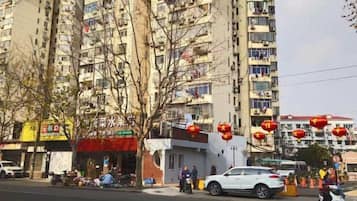 Um edifício residencial com vários andares, varandas, uma rua em frente e lanternas vermelhas.
