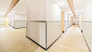 Un pasillo moderno de hotel con piso de madera, paredes blancas y una columna central.