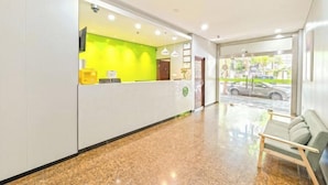 Zona de recepción de hotel con una pared verde brillante, un mostrador de recepción, un área de espera con un sofá y vistas a la calle.