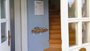 A staircase with wooden steps leading to a landing with a white door and a window. - Haus Hanne Sylt ♡ Holiday home for 6 people for families, 2 generations & dog (Sylt)