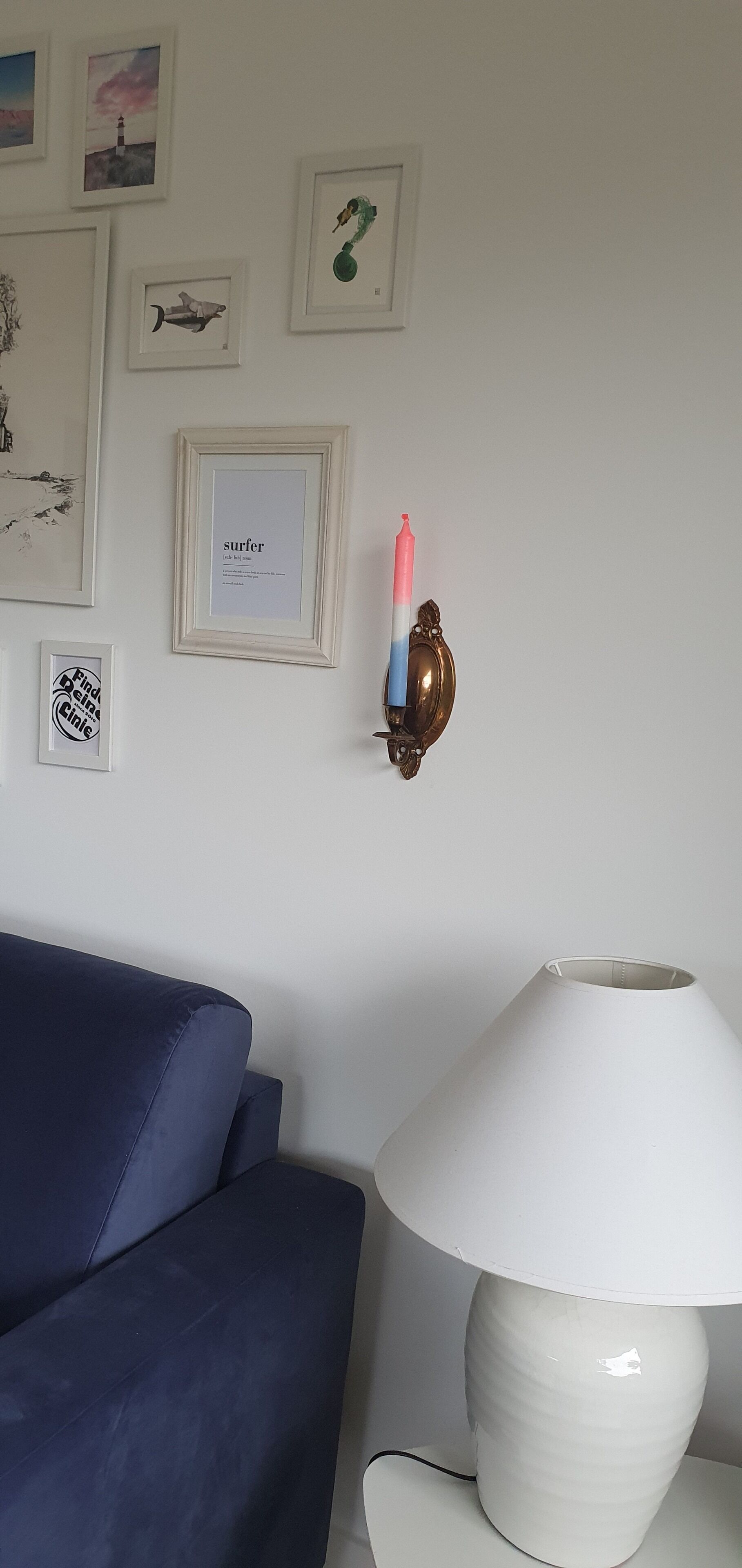 Et værelse med en blå sofa, en hvid lampe og billeder på væggen.