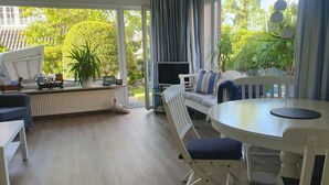 A bright room with a large window, a white table, a white chair, a white sofa, and a radiator. - Haus Hanne Sylt ♡ Holiday home for 6 people for families, 2 generations & dog (Sylt)