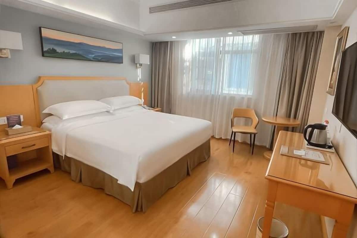 Hotellihuone, jossa on suuri sänky, työpöytä, kahvinkeitin, tuoli ja televisio.