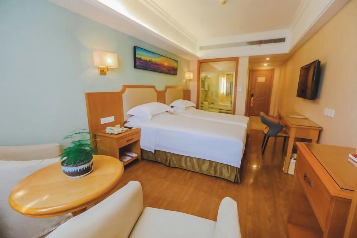 A hotel room with a bed, bedside table, chair, desk, and a TV.