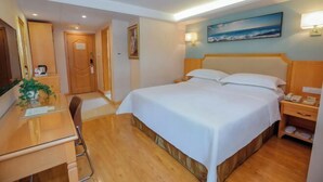 A hotel room with a bed, a desk, a chair, a bedside table, a lamp, and a painting on the wall. - Vienna 3 Best Hotel (Jingmen Wanda) (Jingmen)