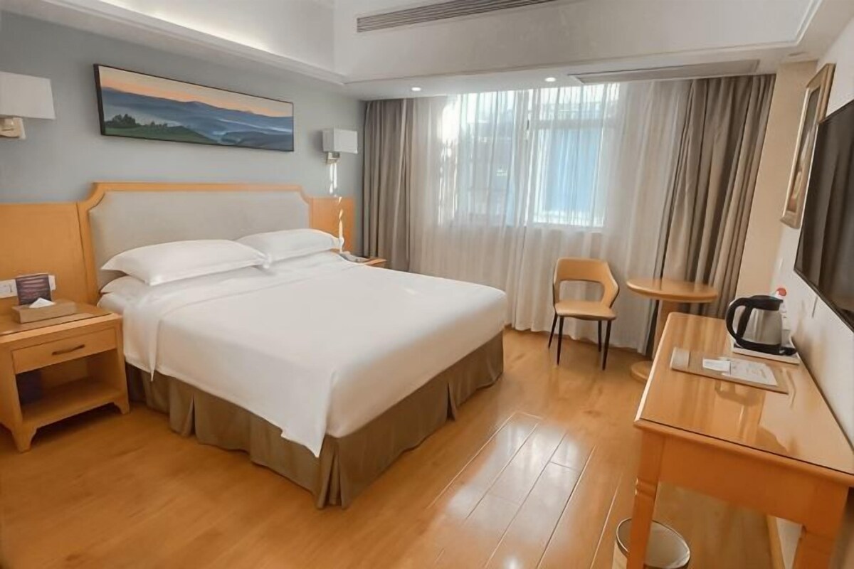 A hotel room with a large bed, a desk with a coffee maker, a chair, and a TV.