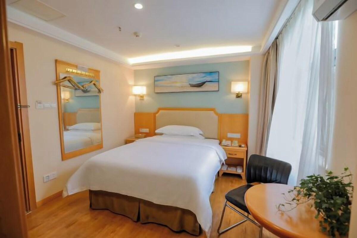 A hotel room with a bed, bedside table, chair, and a window with curtains.