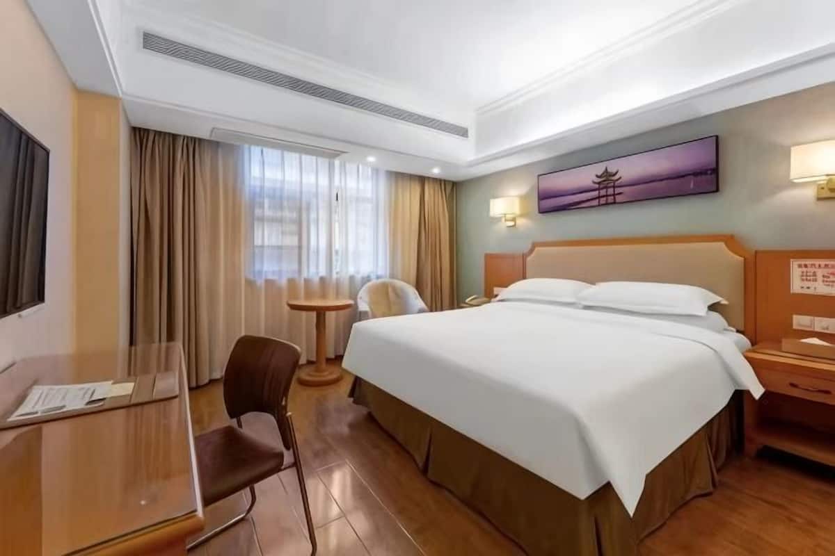 Hotellihuone, jossa on sänky, työpöytä, tuoli, pieni pöytä ja taulu seinällä.