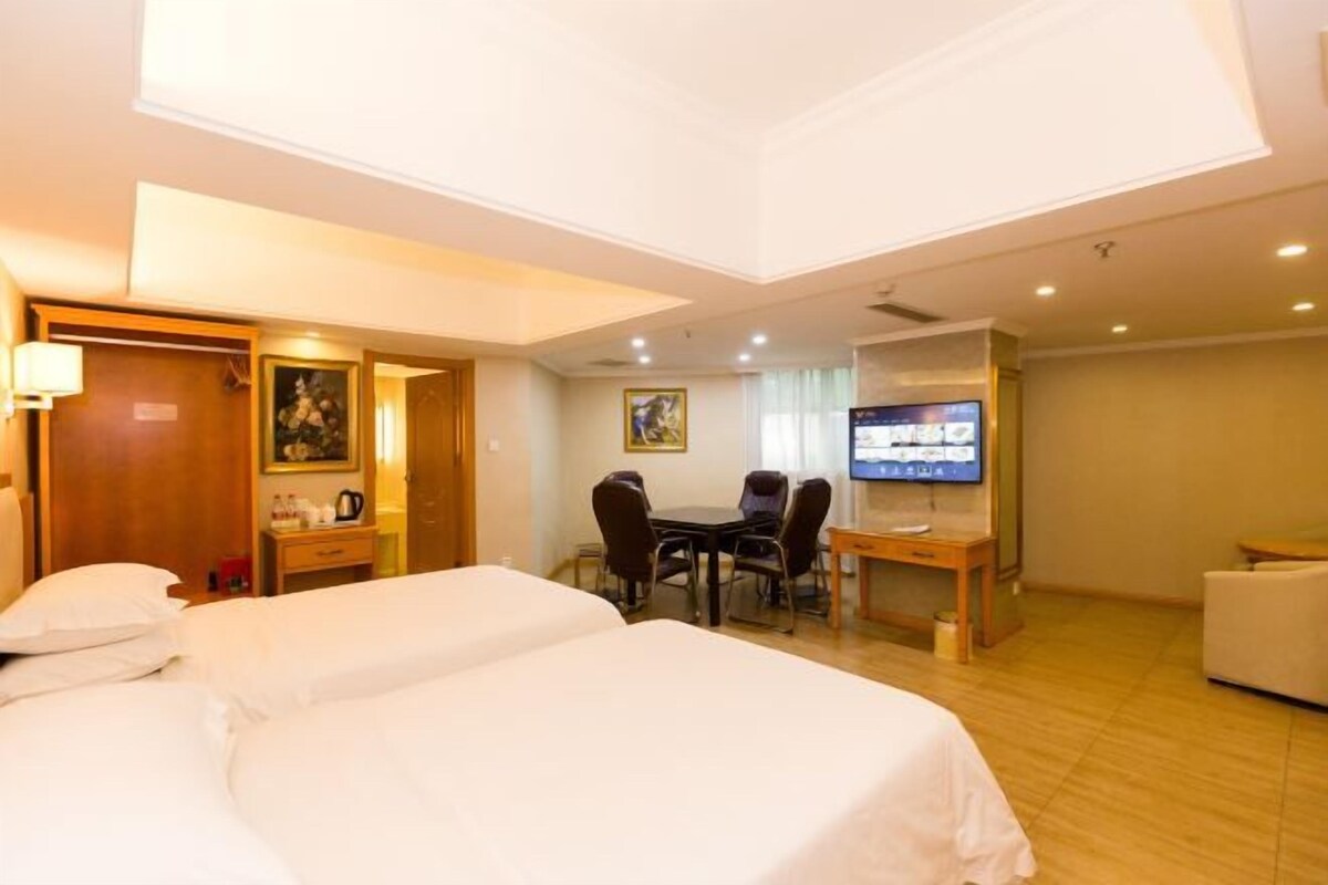 A hotel room with two beds, a desk with a computer, a TV, and a dining table with chairs.