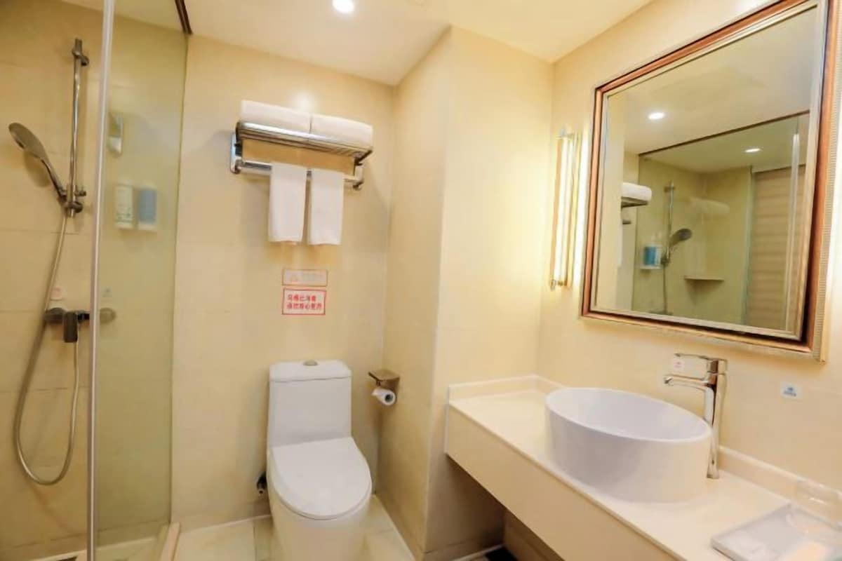 A bathroom with a glass-enclosed shower, a toilet, a sink with a large mirror, and a towel rack.
