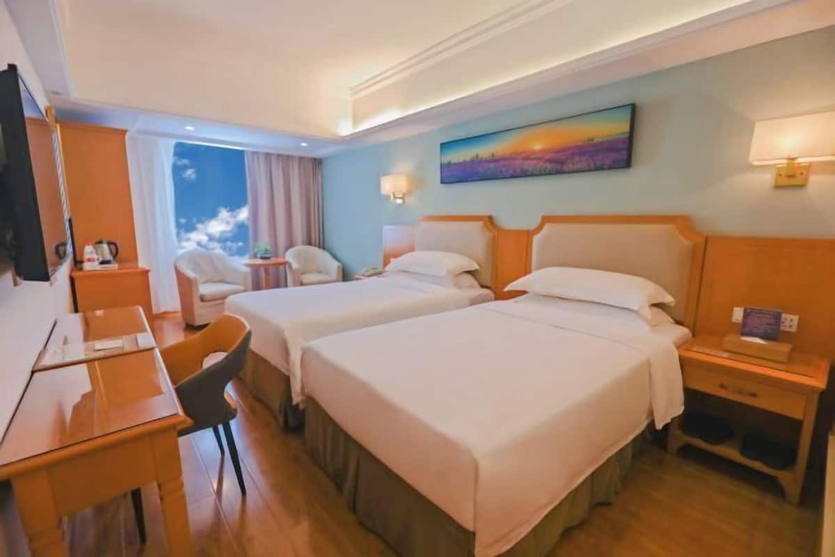 Hotellihuone, jossa on kaksi sänkyä, työpöytä, tuoli, televisio ja taulu seinällä.