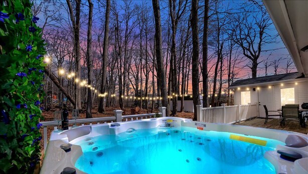 A hot tub surrounded by trees with string lights, set against a twilight sky.