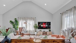 A modern living room with a high ceiling, a large flat-screen TV, and a cozy seating area.