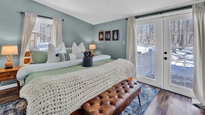 A bedroom with a large bed, a bench, a nightstand, and a view of a snowy landscape through the door.