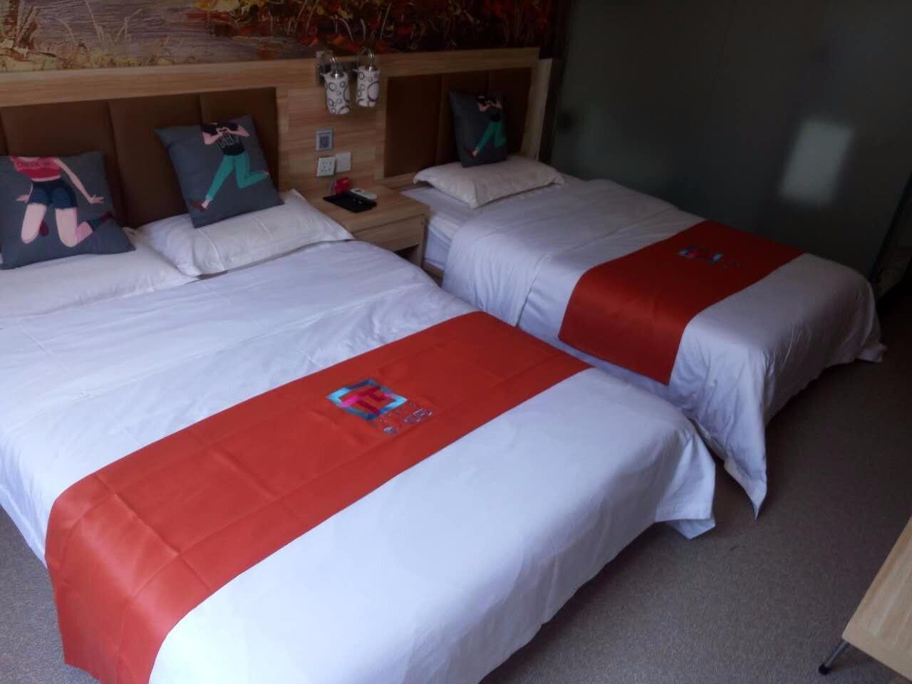 A hotel room with two beds, each with a red and white bedspread, a wooden headboard, and a nightstand with a phone and decorative items.