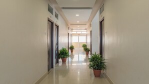 A clean, well-lit hallway with potted plants, doors, and a bright exit at the end. - Hotel Ruchi Shree Garden (Ujjain)
