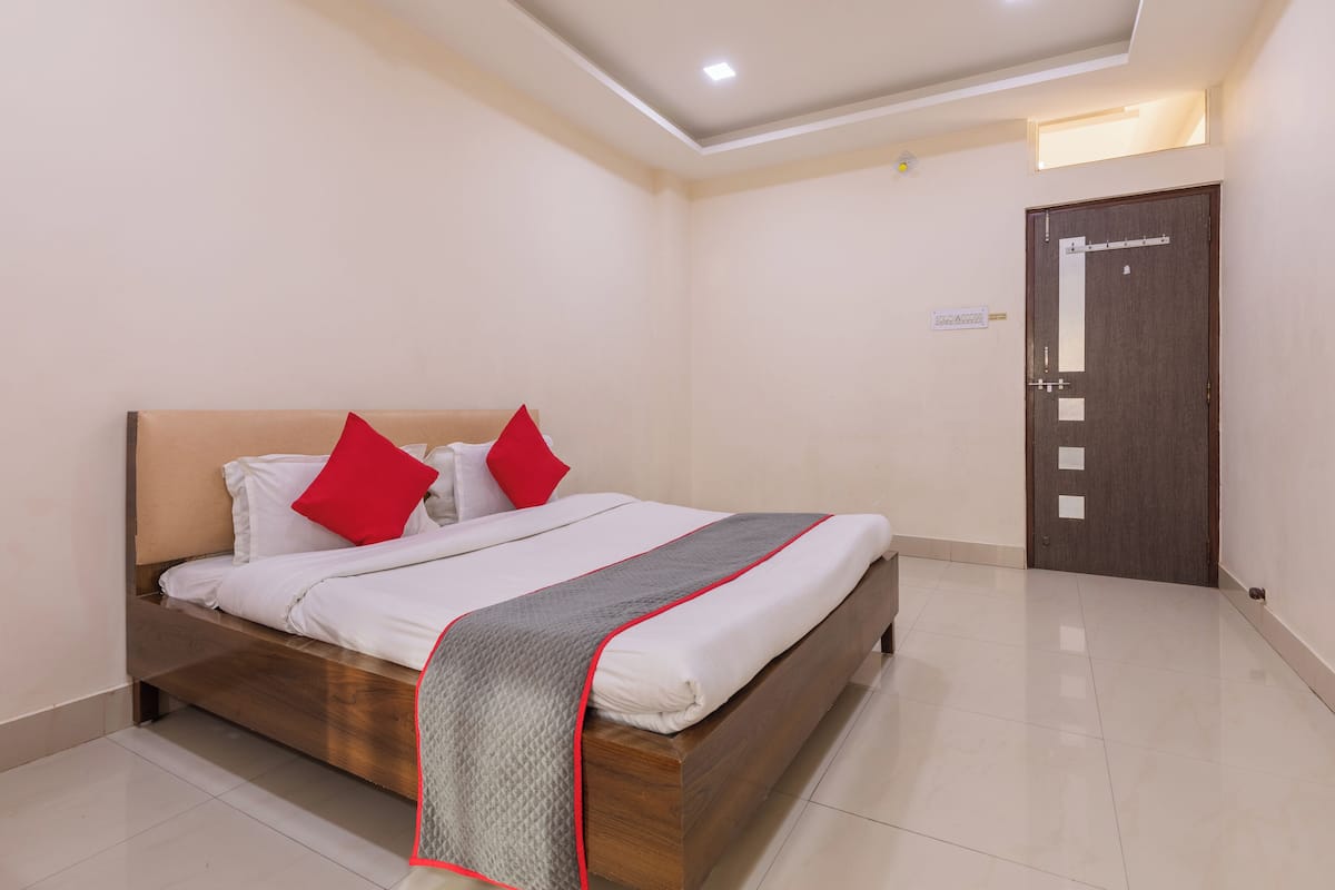 A neatly made bed with a wooden frame, white bedding, and red pillows. There is a door with a sign above it, and the room has a tiled floor.