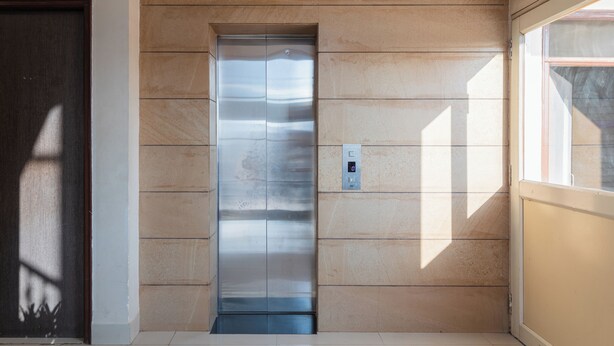 An elevator with a metallic finish, a control panel with a digital display, and a door with a number plate. - Hotel Ruchi Shree Garden (Ujjain)