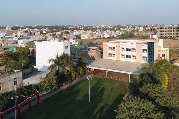 Um edifício de vários andares com telhado e fachada planos, rodeado por vegetação e outros edifícios.