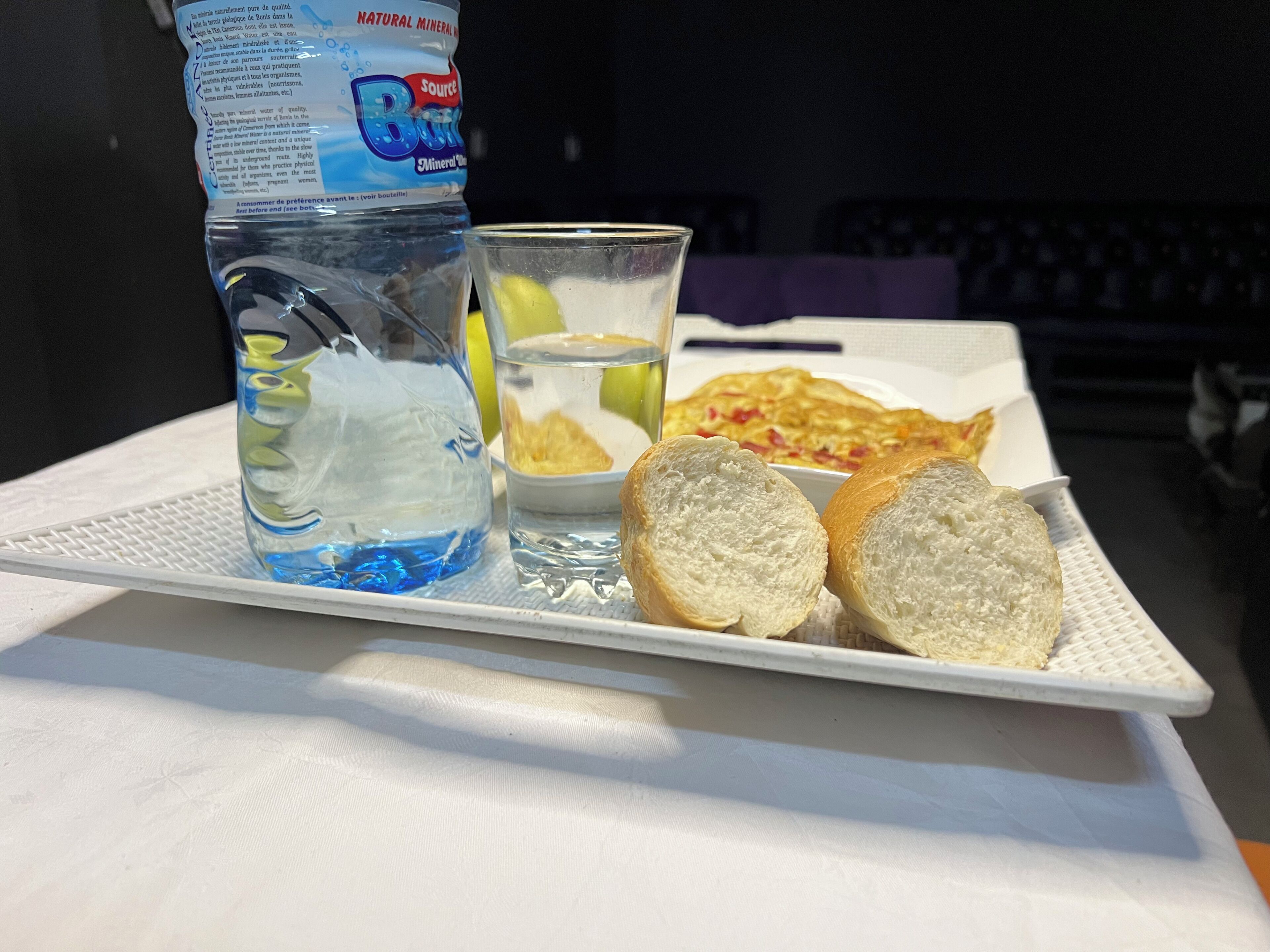 Tarjottimella on valkoinen pöytä, ja sen päällä on vesipullo, lasi vettä sekä kaksi viipaletta leipää.