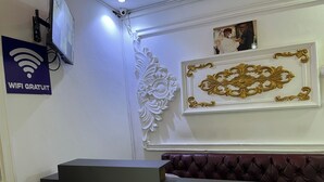 A reception area with a modern desk, a sign indicating free WiFi, decorative wall moldings, and a framed picture above the desk. - Hôtel Famigni (Douala)