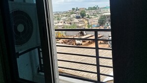 A view through a window with a metal grill, overlooking a construction site with various vehicles and equipment. - Hôtel Famigni (Douala)