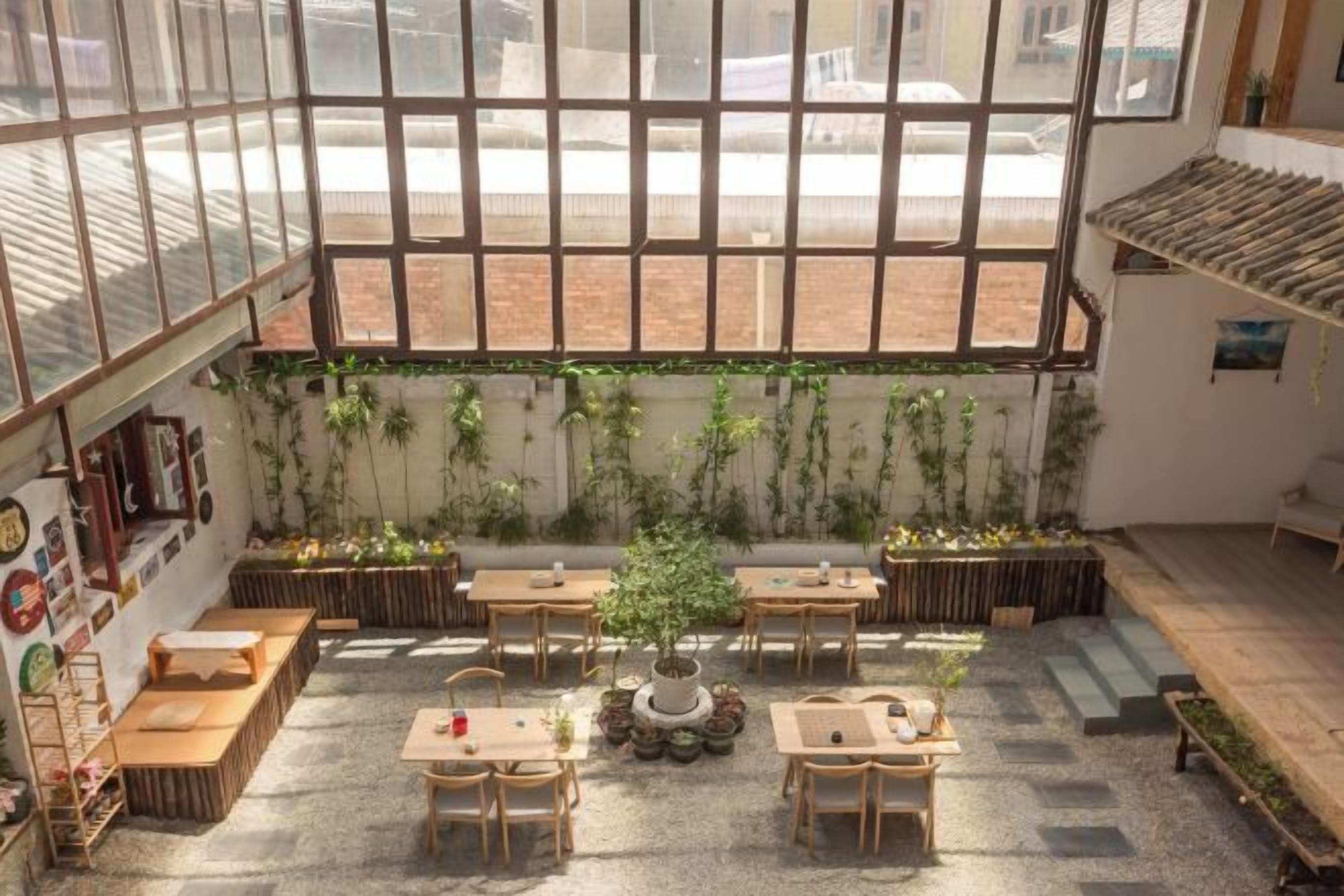 A spacious indoor area with large windows, wooden tables, and potted plants.