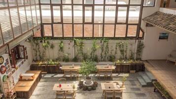 A spacious indoor area with large windows, wooden tables, and potted plants.